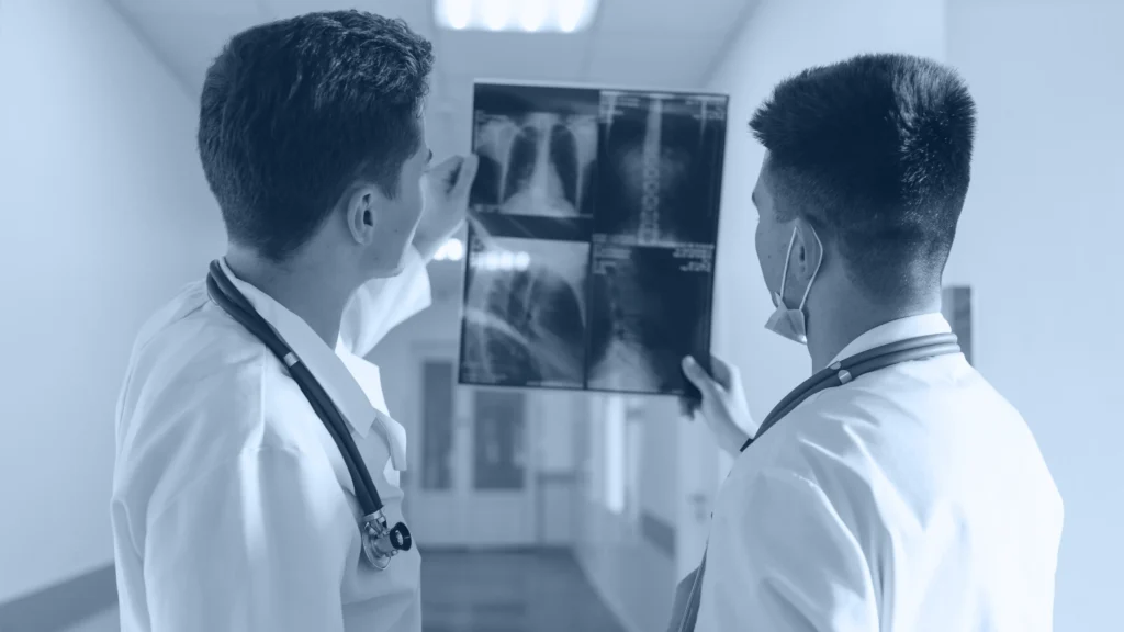 Dos médicos revisando radiografías de columna y tórax en un pasillo