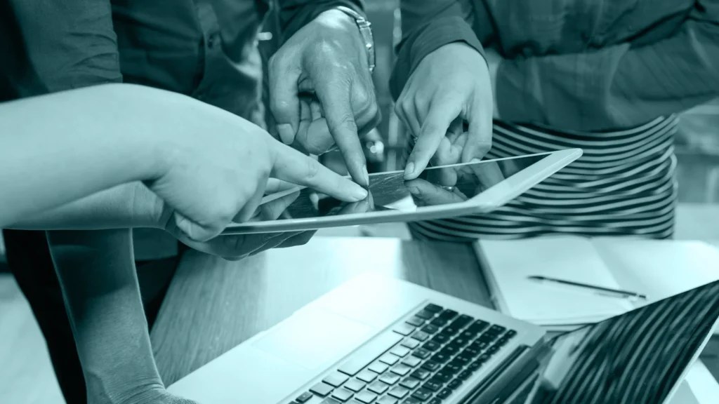 Manos señalando una tablet junto a un notebook durante una reunión
