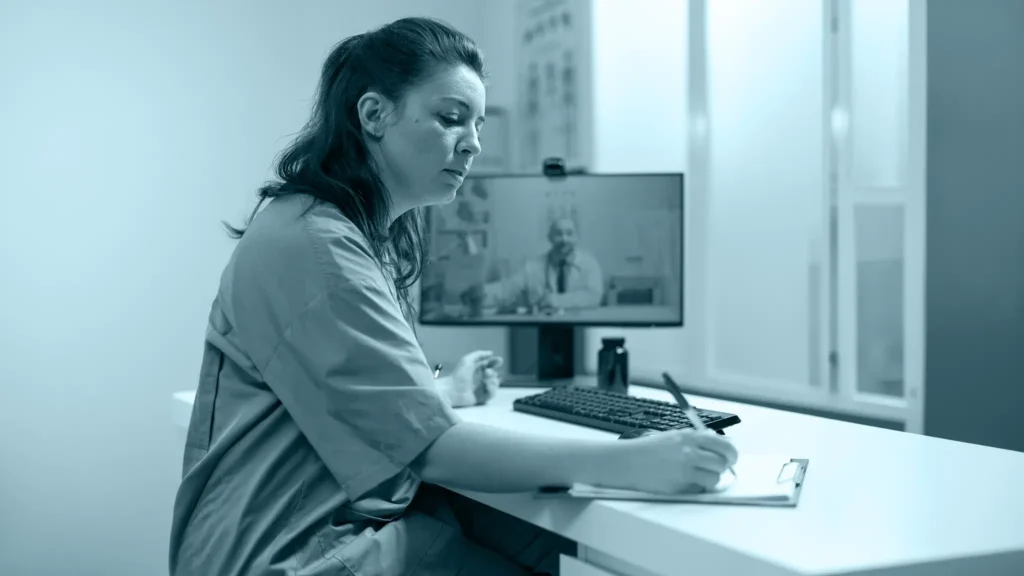 Profesional de salud tomando notas durante una videollamada con un médico