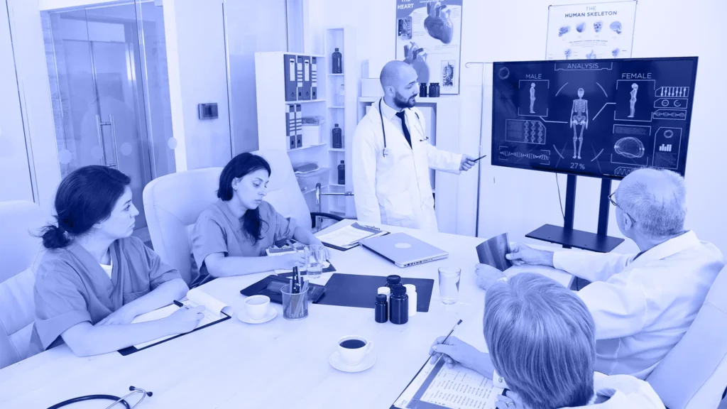 Médico presentando datos clínicos en pantalla a un equipo de salud